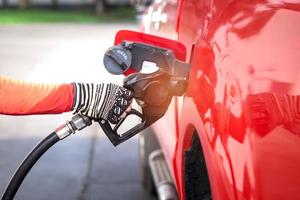 Cierre la boquilla de sujeción de la mano del trabajador para llenar el combustible diesel en el coche rojo en la estación de repostaje foto