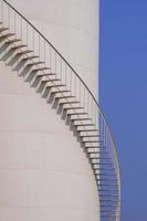 Curved line of spiral staircase on oil storage fuel tank with blue sky in vertical frame
