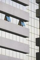 concéntrese en 2 ventanas de vidrio azul que se abren en la pared de un edificio de oficinas de vidrio alto moderno en un marco vertical