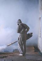 vista trasera de un trabajador de la salud al aire libre que usa una máquina de nebulización que rocía productos químicos para eliminar los mosquitos y prevenir la fiebre del dengue en la zona de tugurios en un marco vertical foto
