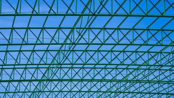 Geometric pattern of green metal  roof structure of industrial building against blue sky background photo