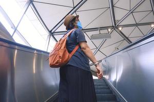 Low angle and rear view of Asian plus size female passenger wears protective mask going up on escalator at subway station, city lifestyle concept photo