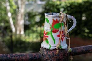 Old dented and painted tankard containing dead daffodils photo
