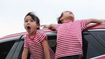 lindas hermanas asiáticas sonriendo y divirtiéndose viajando en auto y mirando por la ventana del auto. familia feliz disfrutando de un viaje por carretera en vacaciones de verano. video