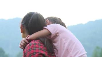 glad asiatisk mamma ger en piggyback-tur till söt liten flicka på sommarparken. mor och dotter går i parken och njuter av vacker vårnatur. video