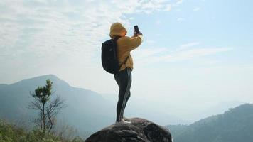 alpinista feminina de pé no topo de uma montanha ao nascer do sol e usando um smartphone. video