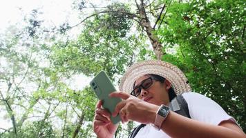 la viajera usa un teléfono inteligente para ubicar y navegar mientras viaja con mochila en un bosque tropical. video