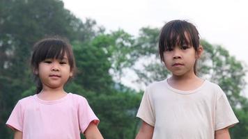 dos lindas hermanas asiáticas tomándose de la mano en el jardín de verano. retrato de dos niñas lindas sonriendo y jugando en el parque. video