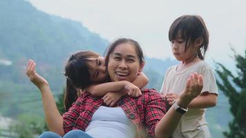 Cute little daughters ran in and hugged the beautiful mother from behind as she sat on the chair with her phone. Mother with pleasure spend time with her child in the spring garden. video