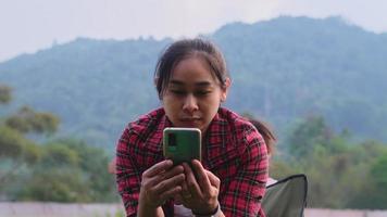 Cute little daughter ran in and hugged the beautiful mother from behind as she sat on the chair with her phone. Mother with pleasure spend time with her child in the spring garden. video