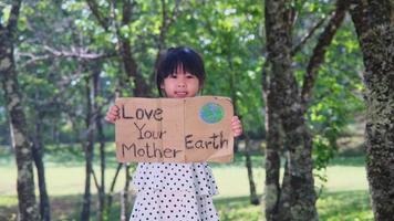 Portrait of cute little girl standing with Love Your Mother Earth poster at the summer park. Children join environmental conservation volunteers. World Environment Day video