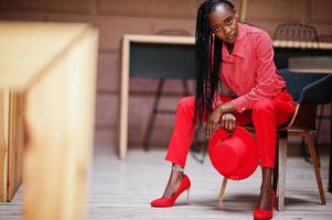 Pretty braids business african american lady bright bossy person friendly wear office red shirt, hat and trousers, sit on chair. photo