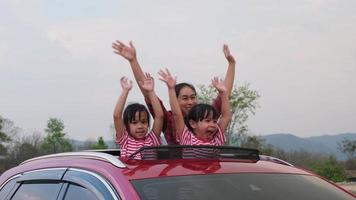 gelukkige familie genieten van road trip op zomervakantie. moeder en kind genietend van de natuur onderweg in de auto op zonnedak. vakantie en reizen familie concept. video
