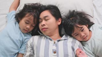 slaperige moeder en schattige dochters knuffelen in bed en zoete dromen. lekker thuis video
