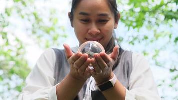 retrato de una mujer asiática sosteniendo una bola de cristal en la mano y deseando un fondo verde de la naturaleza. video