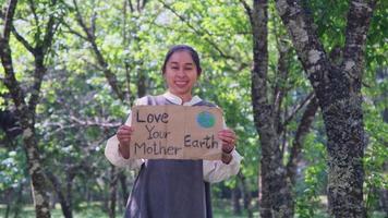 Portrait of woman standing with Love Your Mother Earth poster at the summer park. Female volunteer activists demonstrate protecting the environment. World Environment Day video