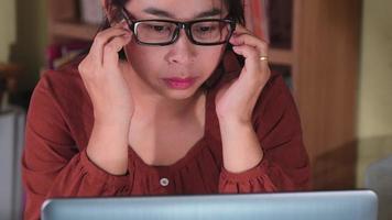 donna asiatica seria che sente mal di testa dopo aver lavorato a lungo sul computer portatile al chiuso. concetto di salute e sindrome dell'ufficio. video