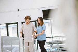 young physical therapist helping senior patient in using walker during rehabilitation photo
