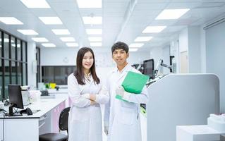 dos jóvenes científicos sonrientes con bata blanca de laboratorio de pie con un analizador de sangre automatizado en un laboratorio médico foto