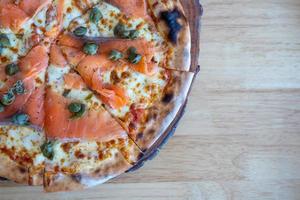 Homemade Smoked Salmon Pizza Topped with Capers, herbs, Dill, Cream Cheese, Tomato sauce and Cracked Peppers. The flatbread with fresh cheese.
