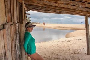 señora de pie fuera de una vieja choza de madera abandonada en praia dos nativos, en trancoso, bahia, brasil foto
