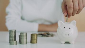 The man is putting two coins into his savings each month. A pig piggy bank holder and is show to the front as a symbol of savings. monthly savings concept. video