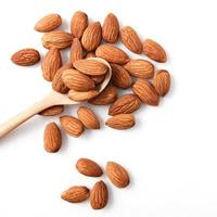 The almonds are in a brown wooden spoon and several seeds around which are on a white background. photo