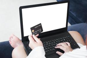 A woman holding a credit card, which is paying online, on a laptop, sitting on the sofa in the living room, at home with clipping path. The concept of online shopping.white screen notebook for mockup photo