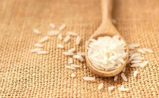 Close up raw rice grain on wooden spoon on sack cloth photo