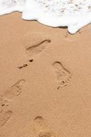 Footprints on the sand of the beach and white color of sea wave bubble photo