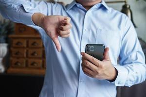 businessman give a thumb down with mobile phone for review product and comment. photo