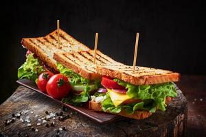 sándwich casero con jamón, lechuga, queso y tomate sobre un fondo de madera foto