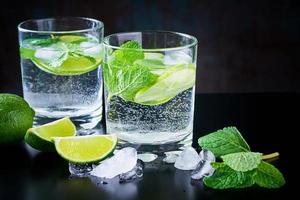 Summer drink lemonade mojito with lime, mint and ice on a black background