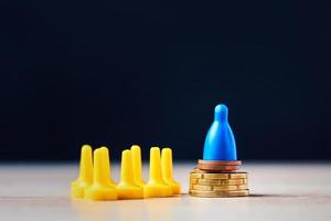 Concept of influence money on people. Figure board game on stack of coins above the group of figures. photo