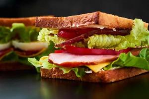 Homemade sandwich with lettuce and ham on a black background, close up photo
