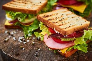 Homemade sandwich with ham, lettuce, cheese and tomato on a wooden background photo