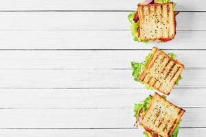 Three sandwiches with ham, lettuce and fresh vegetables on a white background, top view with copy space photo
