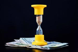 Time is money or time investment and retirement saving concept. Yellow hourglass on pile of dollar bills on a dark background photo