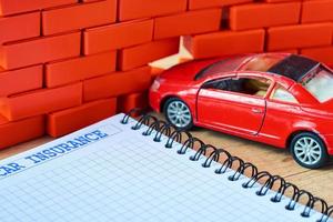 coche rojo en miniatura se estrelló en una pared de ladrillo y formulario de seguro de coche