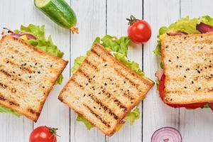 tres sándwiches con jamón, lechuga y verduras frescas en una vista superior de fondo blanco foto