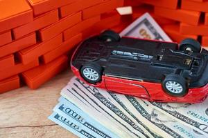 coche invertido en un montón de billetes de un dólar. concepto de seguro de automóvil, daños después del accidente foto