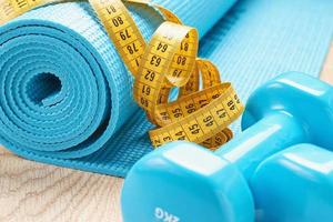 Fitness concept with blue dumbbells, fitness mat and a measuring tape, close up photo
