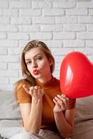 Beautiful woman holding red heart shape balloon sitting in bed