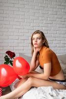 Beautiful thoughtful woman holding red heart shape balloon sitting in bed photo