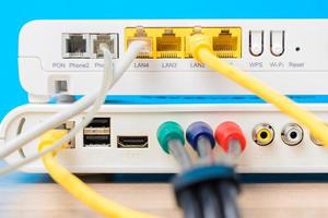 home wireless router with ethernet cables plugged in on blue background, closeup photo
