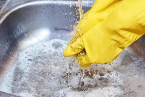 manos con guantes amarillos limpiando el fregadero en la cocina foto
