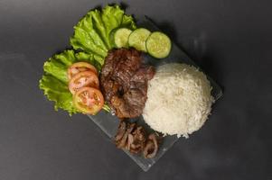 Carne de res a la parrilla con arroz en un plato sobre un estudio de fondo negro foto