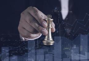 Hand of businessman holding gold king chess on stock market or forex trading graph chart with cityscape image economy trend for digital financial investment.Management or leadership strategy concept. photo