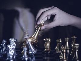 Hand businessman moving the golden knight chess fighting silver knight with fire sparks chess on chess board to successfully in the competition. Management or leadership strategy and teamwork concept. photo