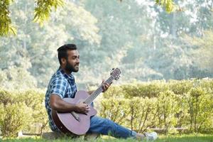 young boy with his guitar and playing guitar in park near tree alone photo